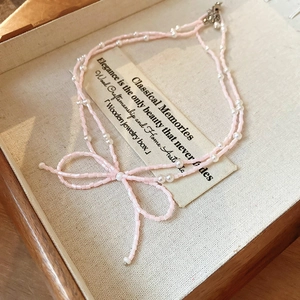 Détail d'un pendentif nœud rose sur un collier double rang en perles et perles rose
