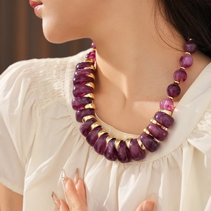 Détail d'un collier de perles mauves et anneaux dorés porté au cou d'un mannequin