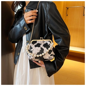 Detail of cow print clasp bag with pearl handle and metal chain strap held by model