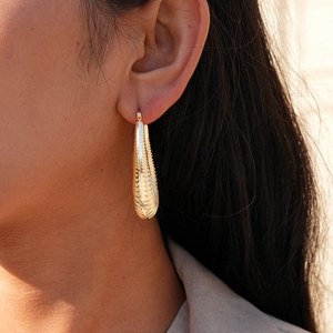 Detailed view of gold teardrop earrings with textured stripes on female model