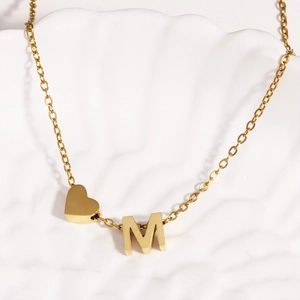 Detailed close-up of 18k gold plated stainless steel heart and letter M necklace on a shell