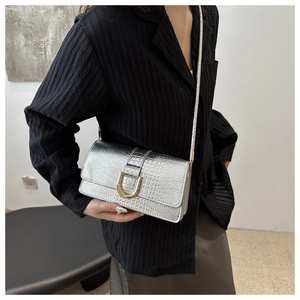 Détail du sac à main argenté motif crocodile avec boucle dorée en U tenu par un modèle