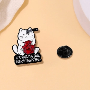 Detail of white cartoon cat enamel pin with a red D20 dice and humorous banner text