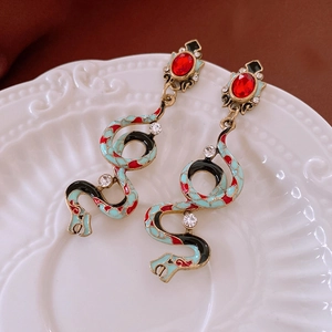 Detail of snake drop earrings featuring turquoise enamel and red gemstones on a ceramic plate