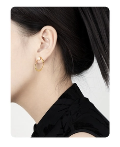 Detail showing an elegant gold openwork earring with a white pearl on a female model