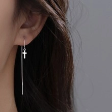 Primo piano di orecchini a catena lunga in argento minimalisti con piccoli ciondoli a croce