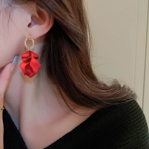 Detail view of a large red petal earring with a textured golden metal stud on a model