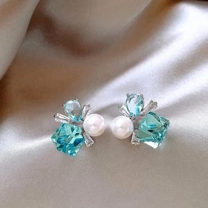 Orecchini geometrici con zirconi blu e perle eleganti su sfondo di seta satinata