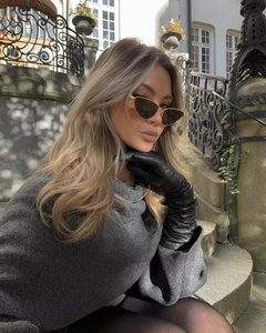 Close-up of elegant black leather gloves and gold frame sunglasses with gray knitwear