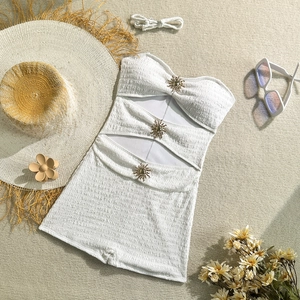 Flat lay of white seersucker one-piece swimsuit with gold sun buckles and beach accessories
