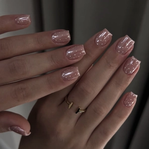 Elegant nude press-on nails with white polka dots and glossy finish for a minimalist look.