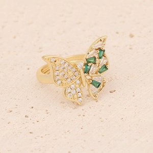 Golden butterfly ring set with green zircon stones on a natural beige stone background