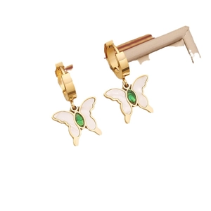 Golden butterfly hoop earrings with white wings and green gemstone center on white background