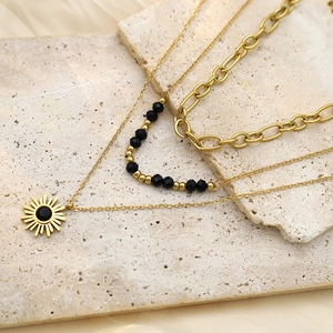 Detailed view of triple-layered gold necklace with black beads and sunburst pendant