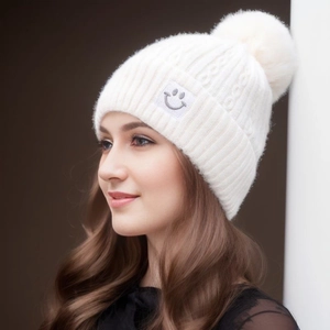 White cable knit beanie with faux fur pom and smiley face patch worn by model