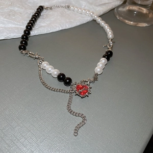 Detail of asymmetrical heart necklace with red gem and thorn silver chain details