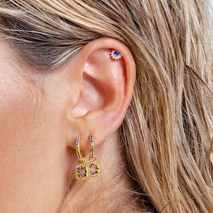 Macro detail of gold-plated geometric earrings with colorful zircons on a model