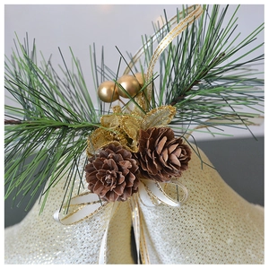Close-up of golden Christmas bells with pine cones, needles, and white ribbon decor