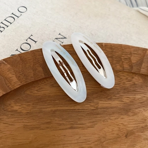 Close-up of white marble acetate oval hair clips with golden French lettering on wood