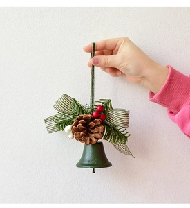 Close-up of green metal Christmas bell with pine cones, berries, and ribbon bow