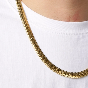 Detail of a gold stainless steel Cuban chain necklace worn by a model on a white T-shirt