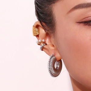 Close-up of stacked gold threaded ear cuffs and textured hollow silver hoop on ear
