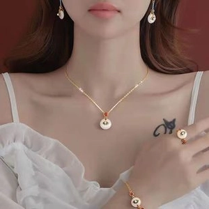 Luxurious gold jewelry set featuring round stone necklace, earrings, and ring on a model