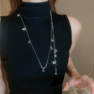 Détail de colliers superposés avec pendentifs en cristal sur un pull en tricot noir