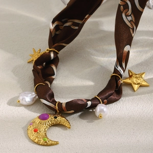 Detail of silk scarf choker with gold moon and star charms on sandy background