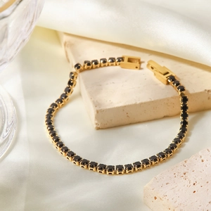 Détail d'un bracelet de tennis doré serti de zircons noirs sur un socle en pierre