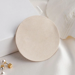 Detail of round beige microfiber jewelry pouch with pearls on white silk background