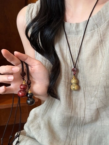 Close-up of wooden gourd pendant necklace with woven cord on a female model
