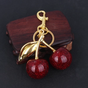 Detail of red glitter cherry keychain with gold leaves on dark wood stand