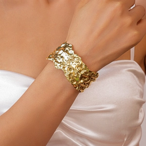 Detail of wide gold open cuff bracelet with irregular hammered lava texture on wrist