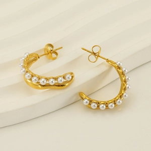 Detailed view of C-shaped 18K gold earrings with white pearls on a textured pedestal
