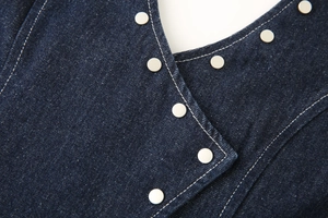 Close-up of deep blue denim fabric with silver metal buttons and white contrast stitching