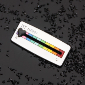 Detail of enamel rainbow mood tracker brooch with sliding heart on black sand base
