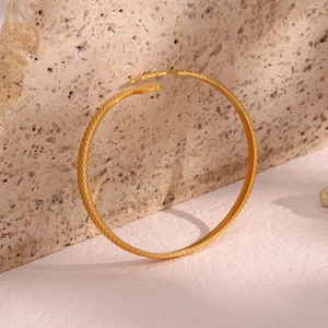 Macro detail of golden snake-textured open bangle bracelet on textured stone background