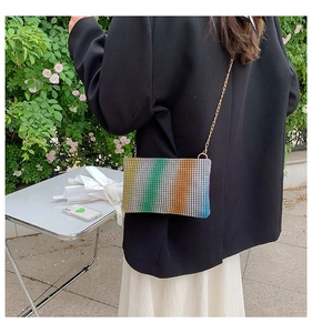 Close-up of a rainbow rhinestone envelope bag with a delicate gold chain strap on a model