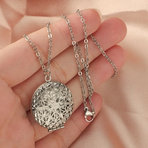 Collier médaillon rond en acier inoxydable 316L avec motif fleuri évidé tenu en main