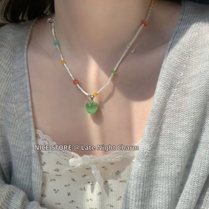 Detail of sweet green apple pendant on a colorful beaded necklace worn by a model