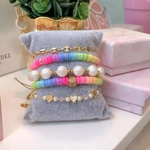 Detail of colorful stacked bracelets with rainbow clay beads and pearls on a velvet pillow