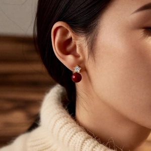 Close-up of a model wearing a star-shaped gold earring with a red pearl drop