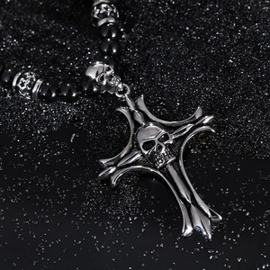 Detail of silver skull cross pendant with black beaded chain on dark textured background