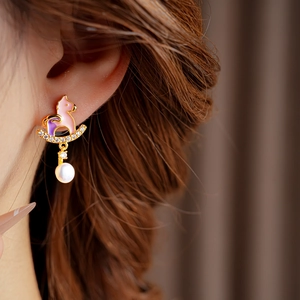 Detail of golden rocking horse earring with enamel colors and a hanging pearl on ear