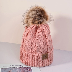 Close-up of pink cable knit beanie featuring a large faux fur pompom and leather brand logo