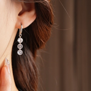 Macro shot of silver drop earrings with three cubic zirconia stones worn on ear