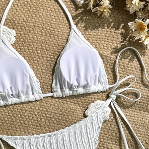 Close-up of white textured bikini with ruffle edges and halter neck detail on straw mat