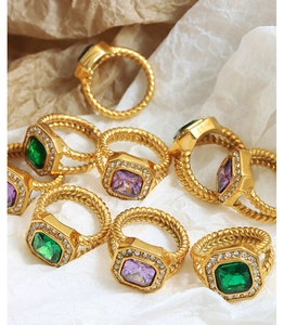 Macro shot of twisted gold rings with green and purple square gemstones on textured paper