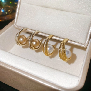 Detailed macro view of C-shaped gold pearl earrings with micro-pave diamond accents